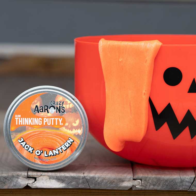 Tin of Jack O Lantern Thinking Putty® next to an orange pumpkin bucket.