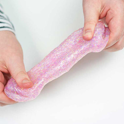 Two hands resting on a white color surface stretching pink sparkle putty.
